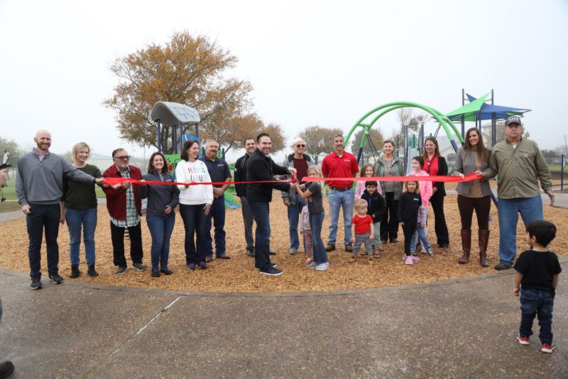 Group of people, including children, cut a big red ribbon in front of a playground structure