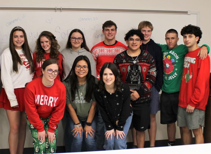 Eleven teenagers, some of them wearing Christmas shirts and sweaters, pose for a photo