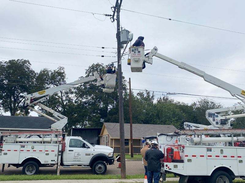 Two cherry-picker style trucks lift technicians to a streetlight mounted on a power pole