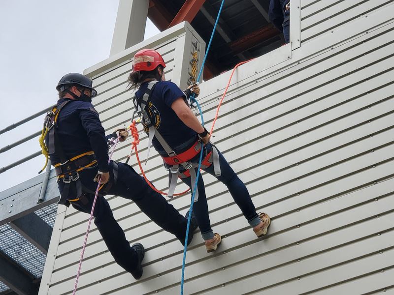 Two people rappel down the side of a metal building