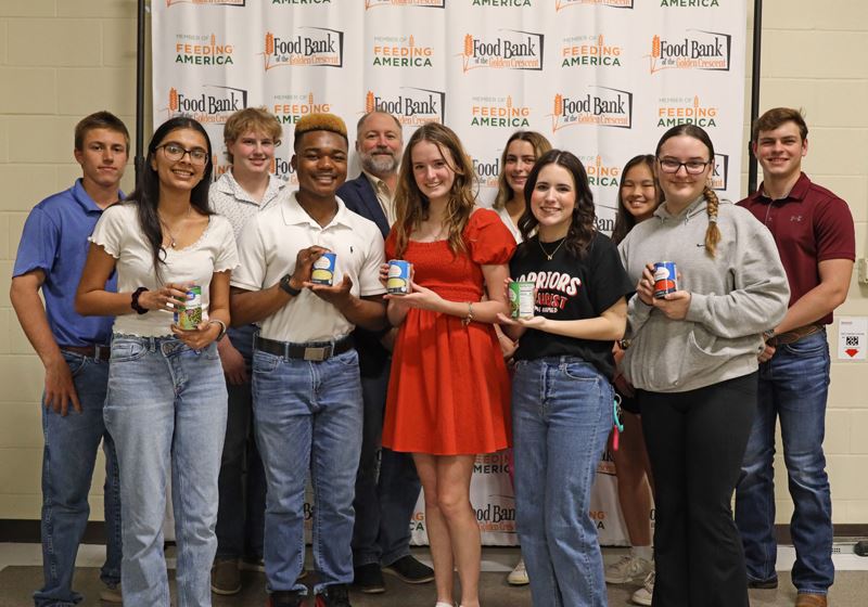 Mayor Jeff Bauknight and a group of teens holding canned food pose in front of a food bank backdrop