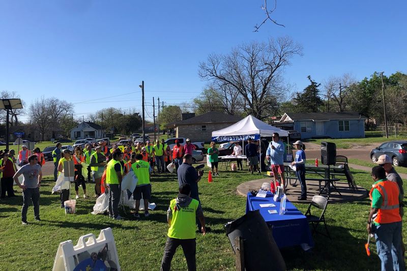 People in safety vests gathered in a park. A registration booth stands in the corner of the block.