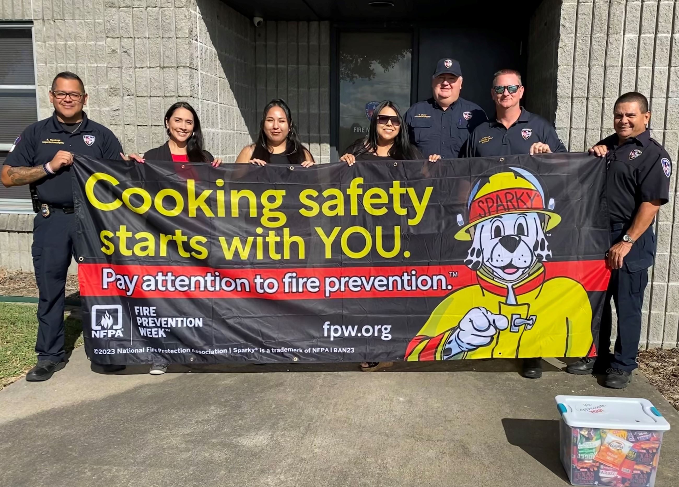 Seven people, some in fire department dress shirts, hold a Fire Prevention Week banner
