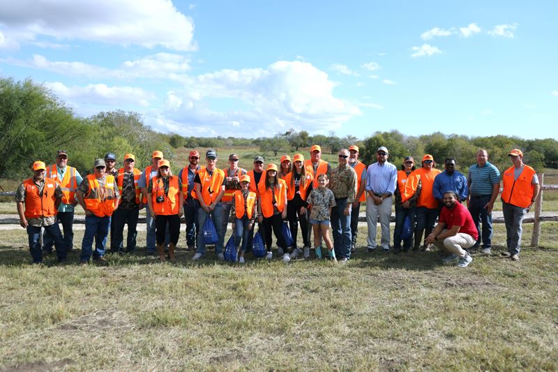 Large group photo of kids and adults, many wearing orange safety vests for huntin.