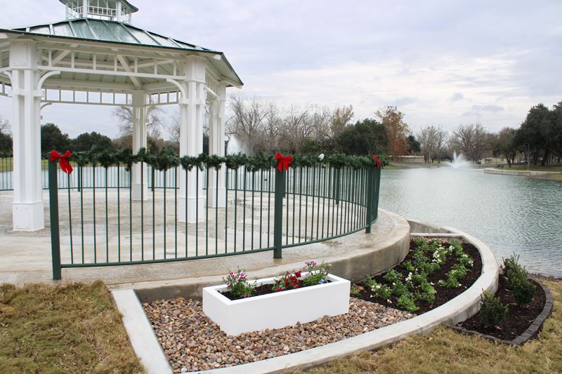 A gazebo overlook with railing lined by Christmas garland and surrounded by planter boxes