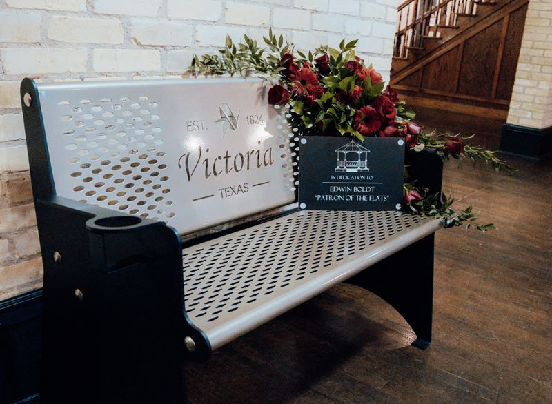 A metal bench. A plaque propped up on the bench has the Main Street logo and a sample inscription.