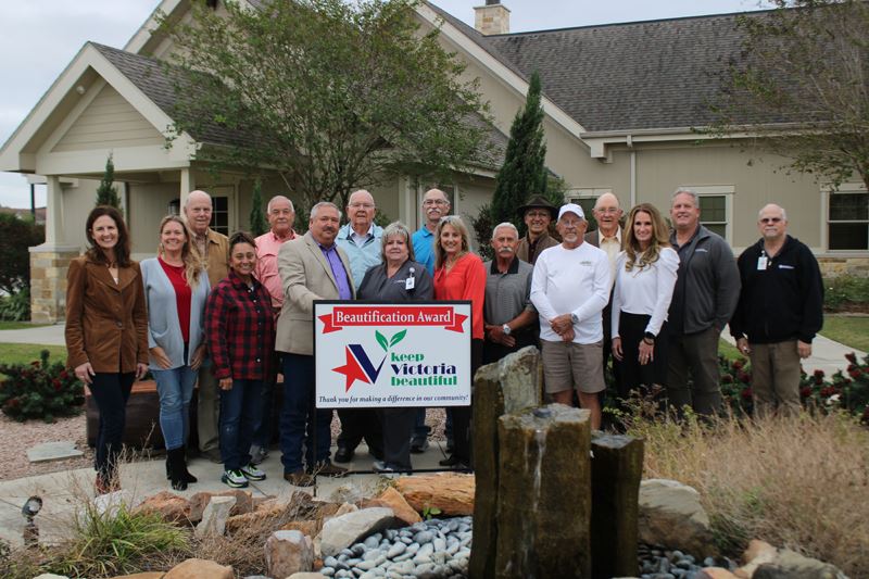 Group photo with KVB sign near a fountain in a small courtyard surrounded by decorative plants.