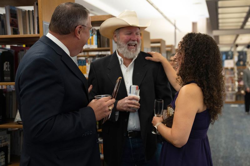 The mayor and two other people talking and laughing while holding drinks at the library