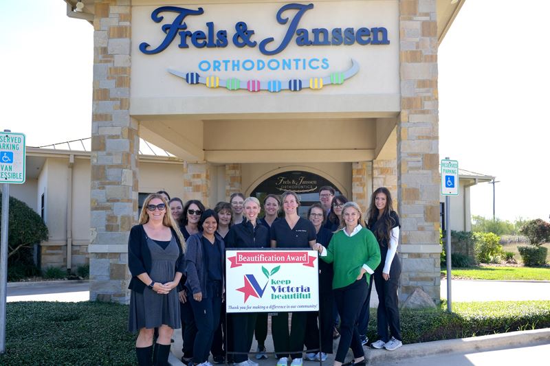 Group photo with KVB sign in front of a facade with brick columns & sign with illustration of braces