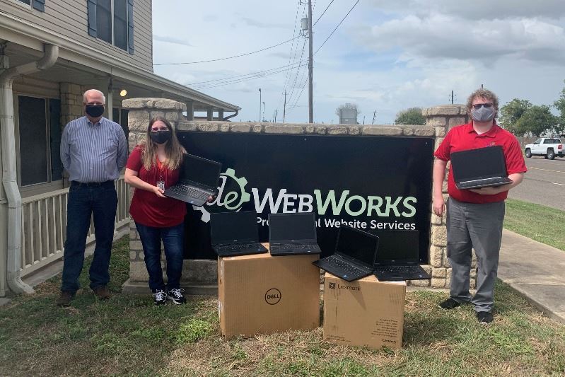 City staff, DE Webworks representative pose at DE Webworks sign with donated laptops