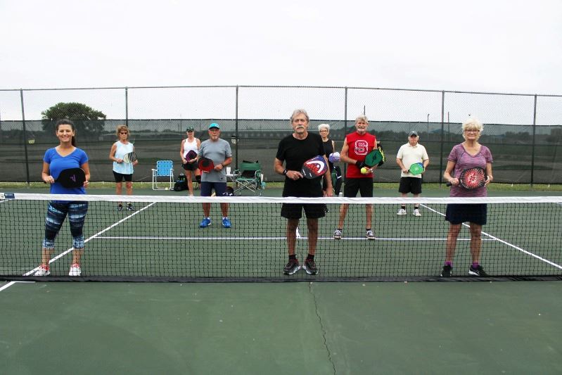 Pickleball players stand at a distance from each other on a pickleball court.
