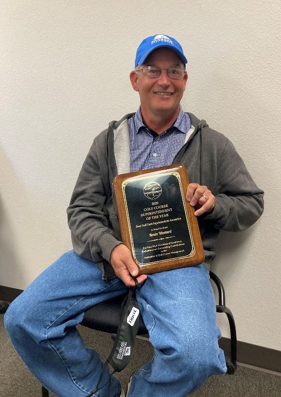 Riverside Golf Course Superintendent Brian Woolard, seated, poses with plaque