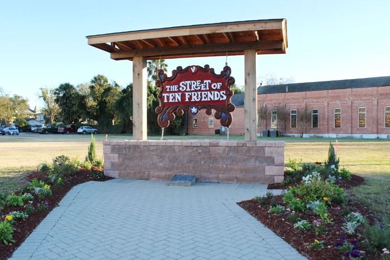 Large wooden hanging Street of Ten Friends sign is surrounded by flowers and shrubbery