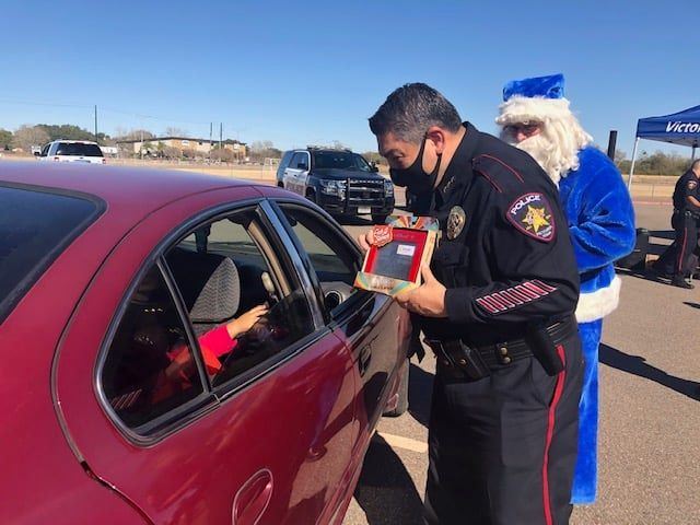 Uniformed police chief hands a gift-wrapped Etch-a-Sketch to a child through a car window.