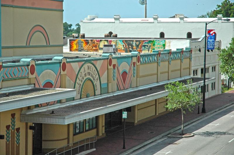 Elevated view of the Leo J. Welder Center building. A Main Street banner and street art are visible.