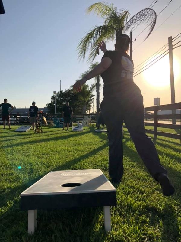 Woman is silhouetted throwing a cornhole bag during a game of cornhole outside in the evening.