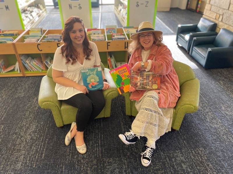 Two women sitting in library children's section holding children's books