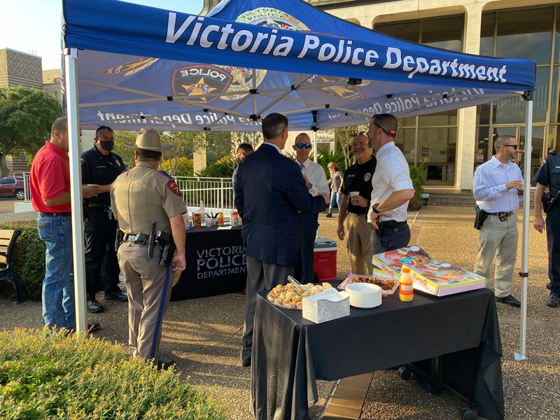 People talking under an outdoor canopy that says Victoria Police Department. Snack table in front.