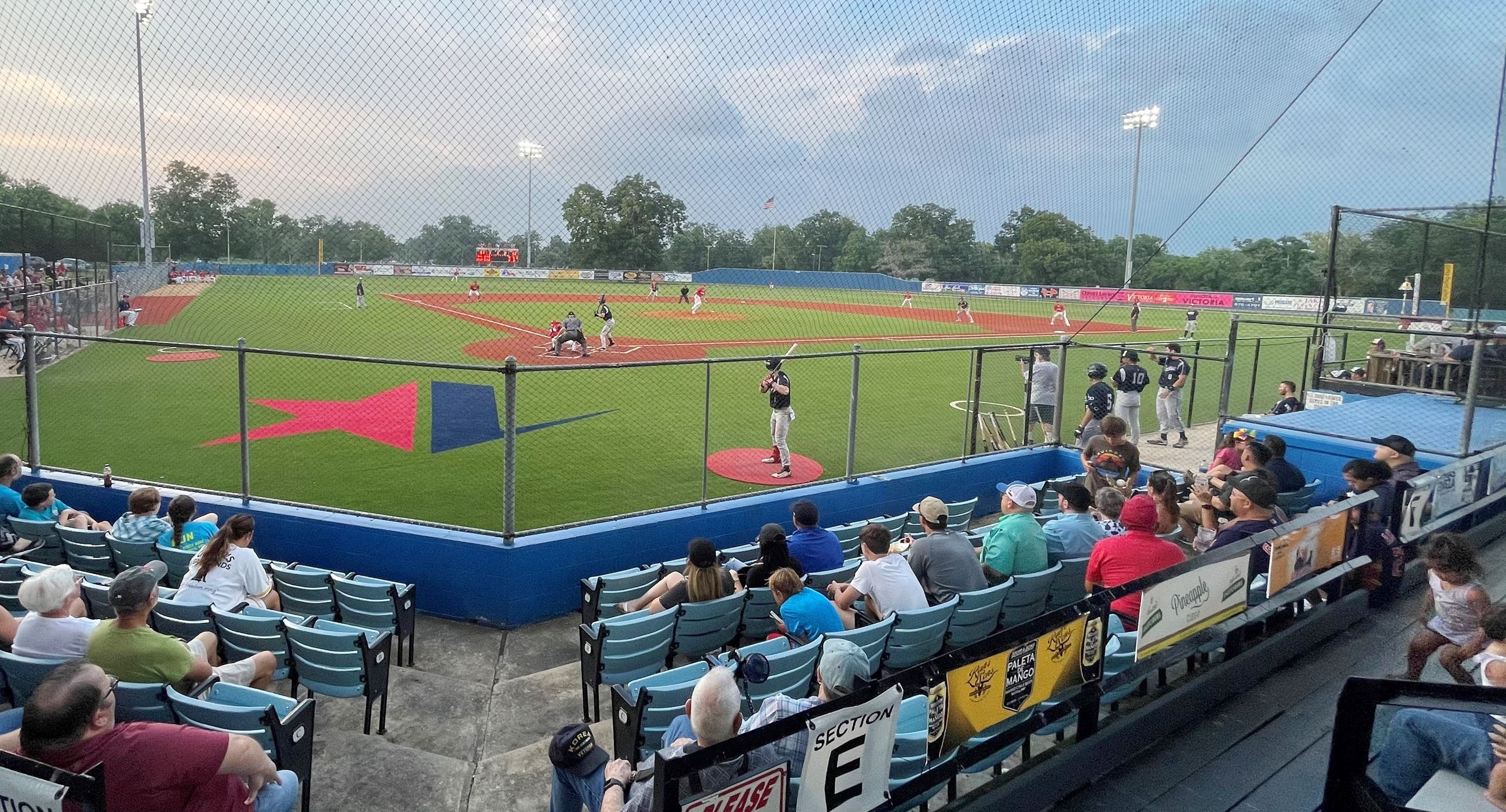 Baseball game at Riverside Stadium. People sit in stands. 2 children move about in the aisles.