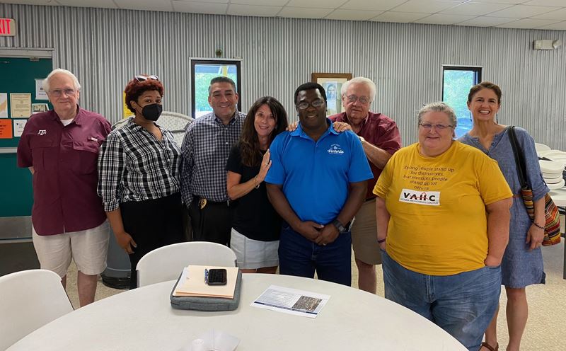Group photo of people standing around a foldout dining table in a building with sheet metal walls
