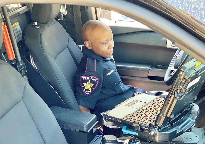 Young girl in police uniform sits at the wheel of a police car and looks at a computer display.