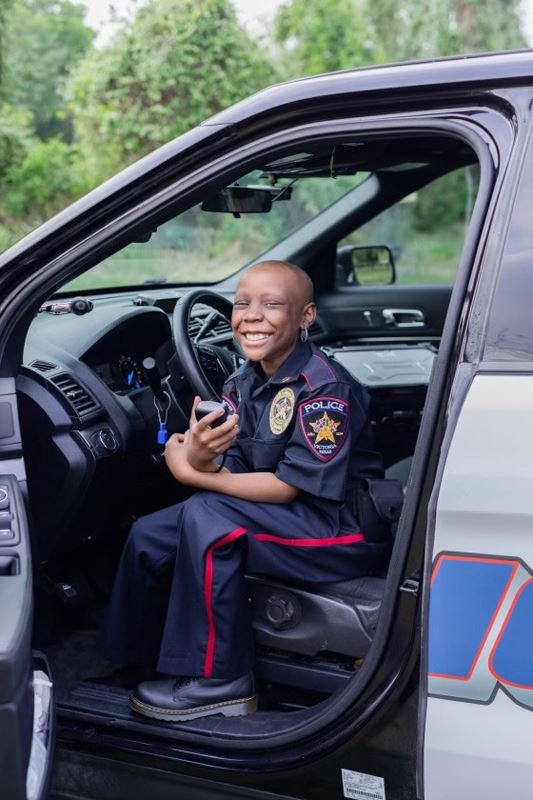 Young girl in police uniform sits at the wheel of a police car