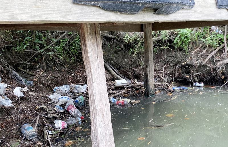 Plastic bottles, soda cans and other trash on the Guadalupe River bank underneath a wooden pier