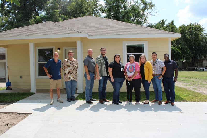 Group photo in front of a newly built house. Yellow with white trim.