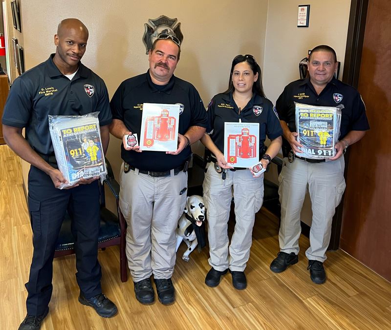 Four people in Victoria Fire Department polos hold packages containing flyers and crafts for kids