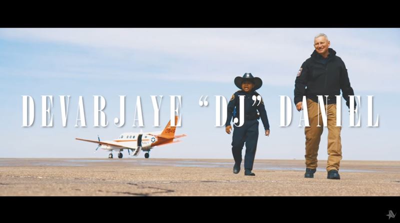 A man and a boy in a cowboy hat walk away from a small plane. Title text reads Devarjaye DJ Daniel