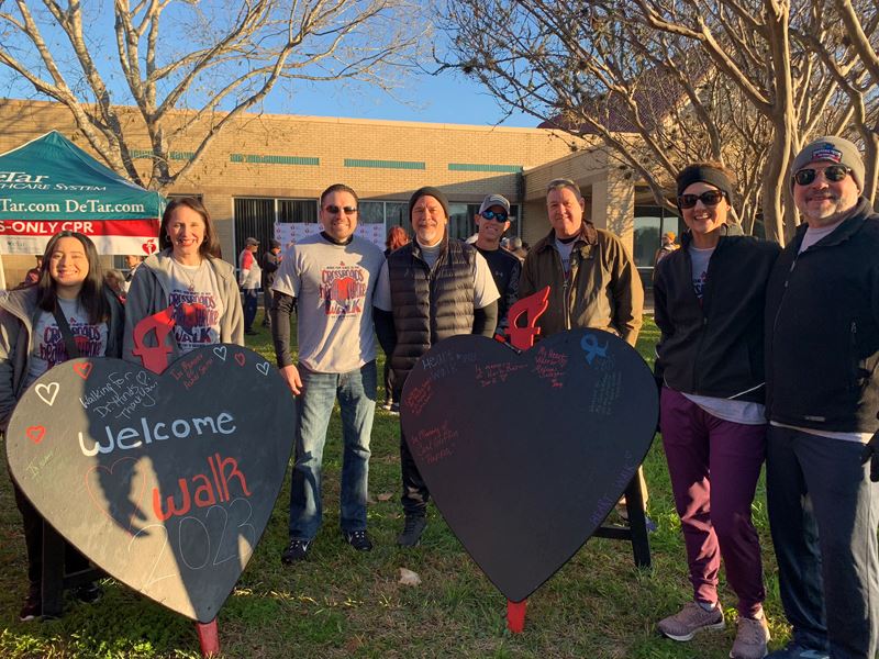 Group of people in light jackets pose outside with 2 decorative hearts with messages written on them Opens in new window