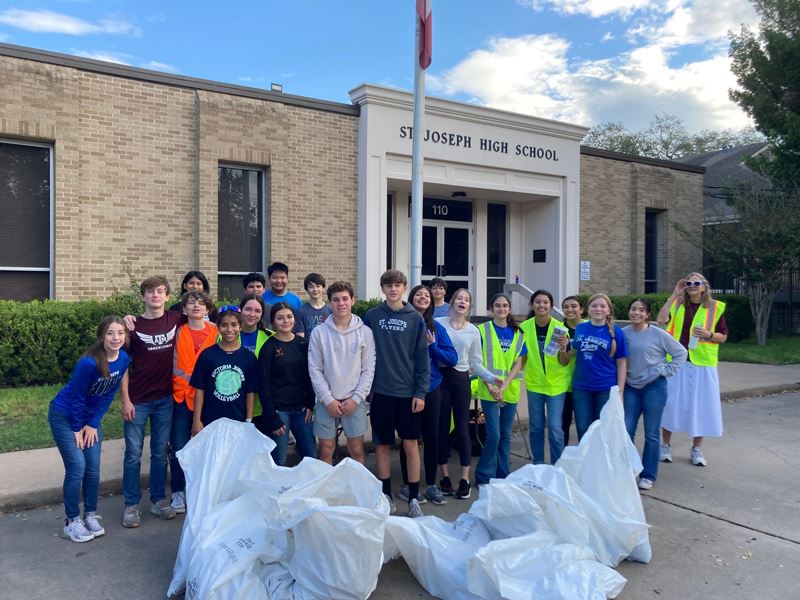 Teenagers pose with bags of trash in front of St. Joseph High School