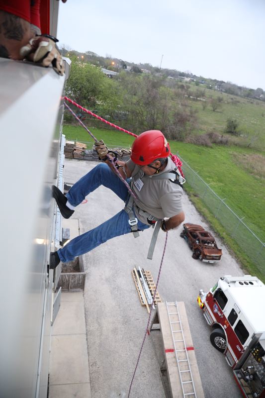 Person wearing a helmet rappels down a building