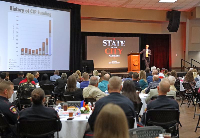 Mayor addresses a large audience while consulting a graph of CIP funding on a large screen Opens in new window