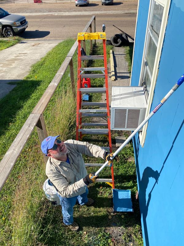 A man uses a paint roller to paint a house blue