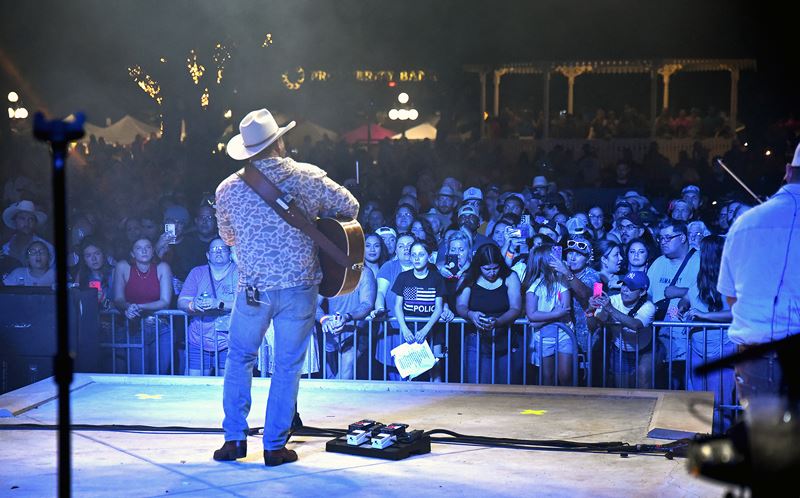 A band with a guitar player in a cowboy hat facing a large crowd at De Leon Plaza