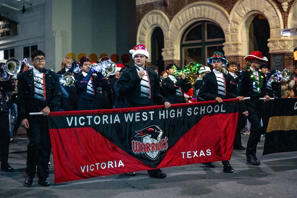 Victoria West High School band marching in a parade and carrying a banner