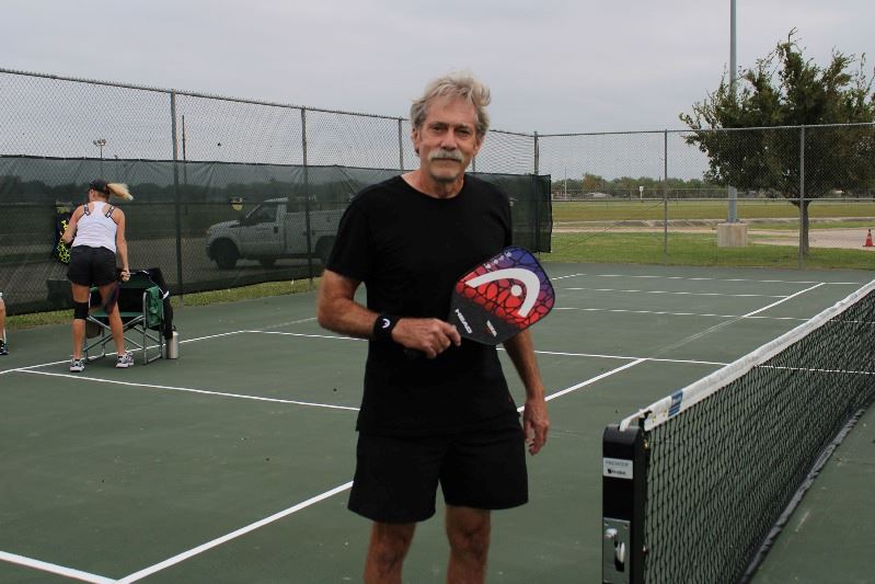 Man poses on a pickleball court with a pickleball racket