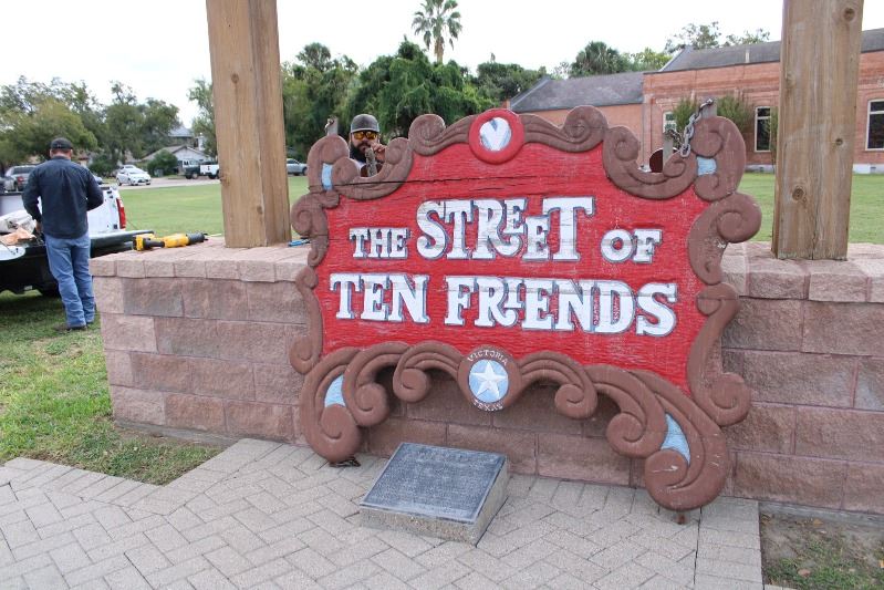 A weathered wooden sign with peeling paint sits near an empty roofed area where a sign could be hung
