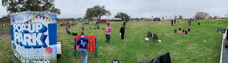 People of all ages play with giant Connect Four set, cornhole boards and other items in a wide field