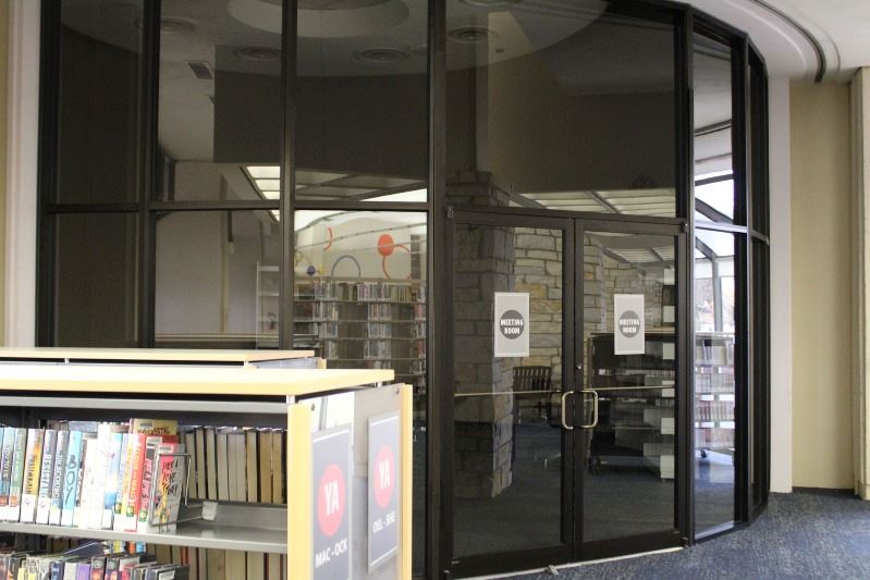 A glass-walled room in the corner of the library. The lights are off in the room.