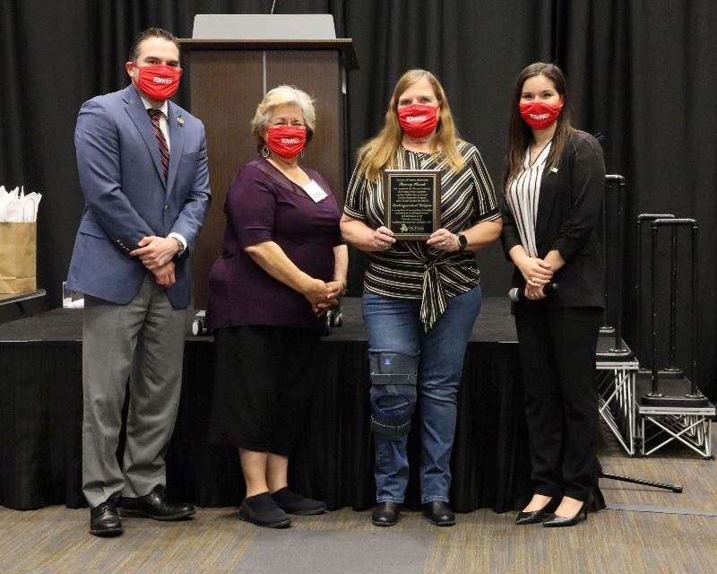 Woman holding plaque poses with three other people.
