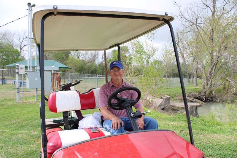 Man in a ball cap sits in a red  Gator-style ATV on a golf course.