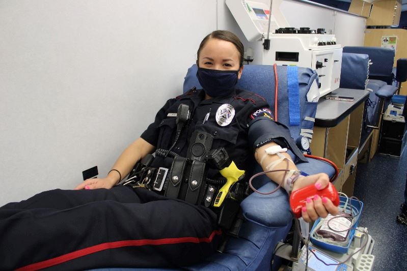 Woman in police uniform is hooked up to blood donation equipment.