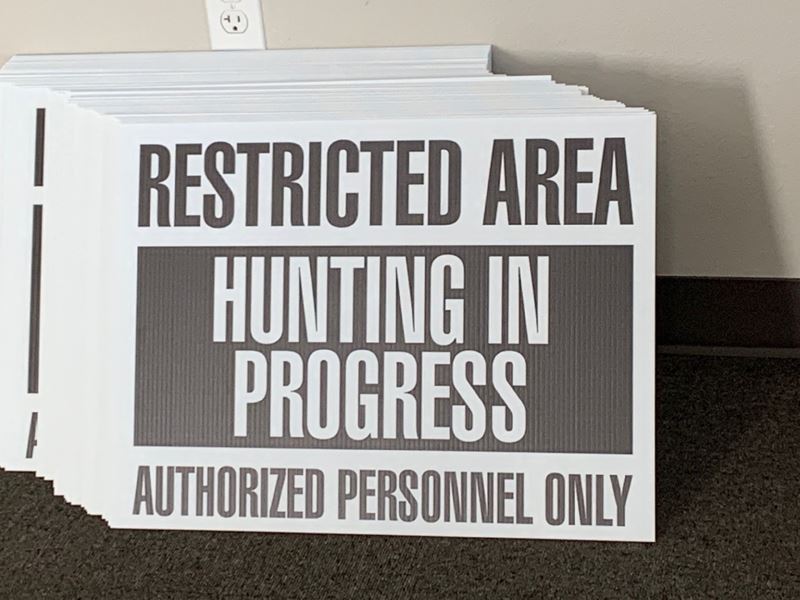 A stack of signs reading "Restricted area, hunting in progress, authorized personnel only."