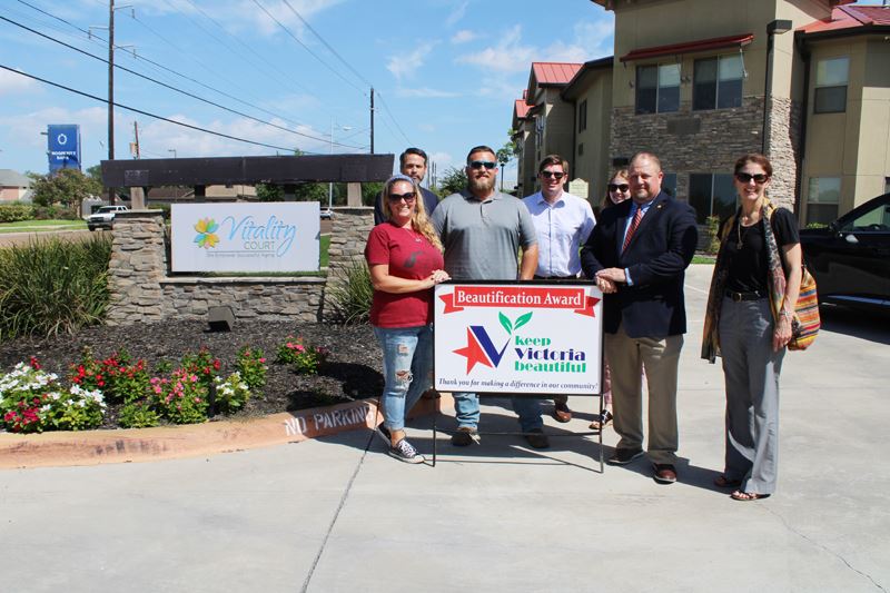 Group photo with KVB award sign in front of Vitality Court sign and flowerbed